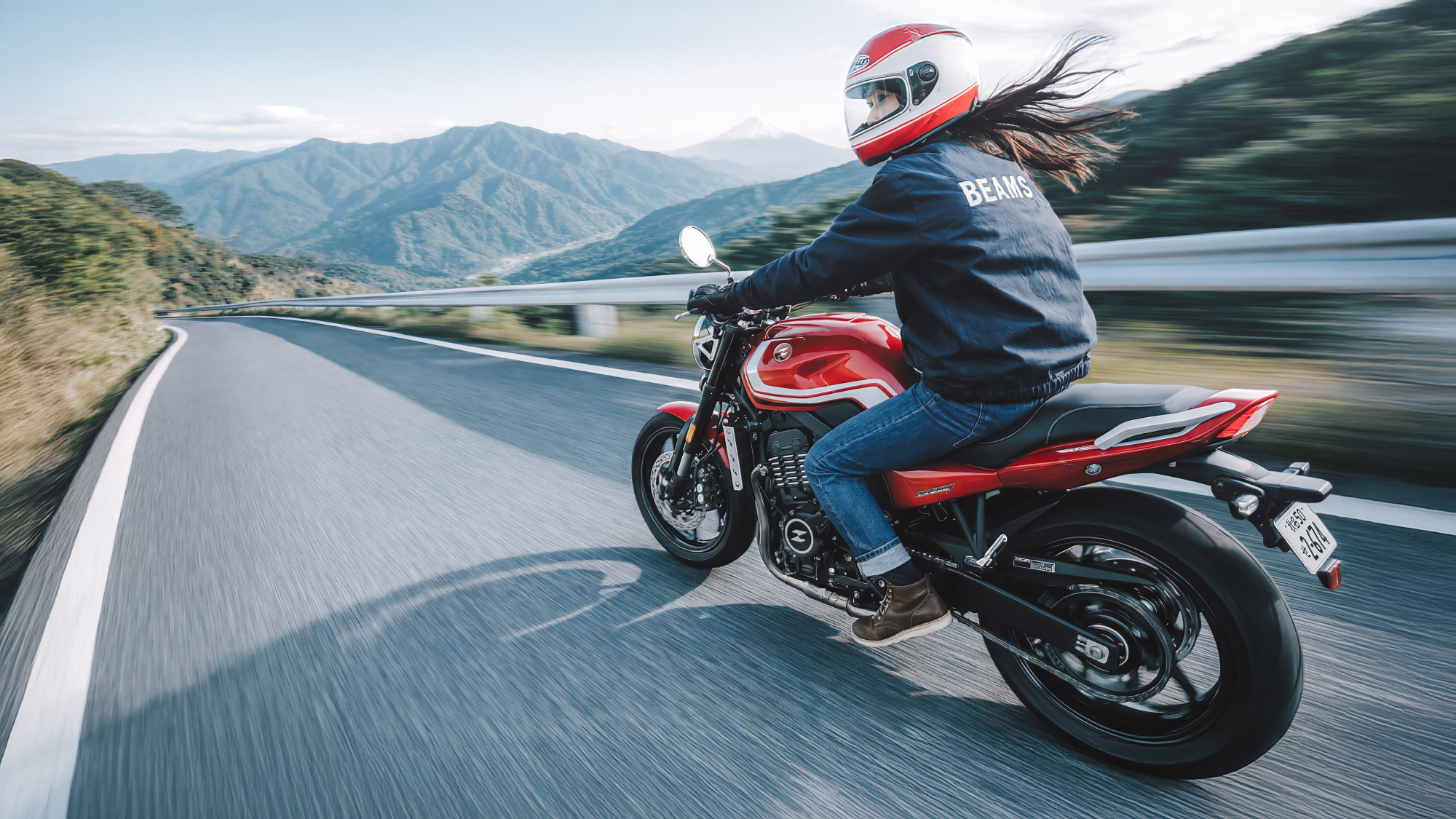 ZXMOTO 500F | Red Motorcycle on a Mountain Bend Rear three-quarter view of a rider on a red 500F following a mountain road beside a metal guardrail.