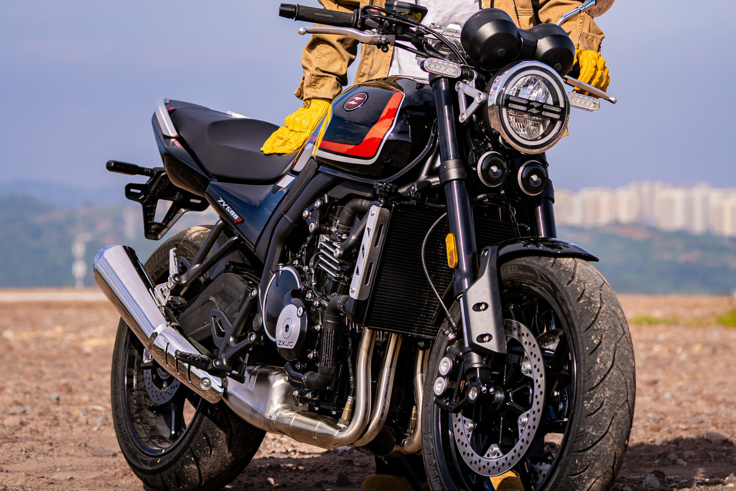 Black and red ZXMOTO 500F with a round headlight and silver exhaust, with a rider wearing yellow gloves behind it.