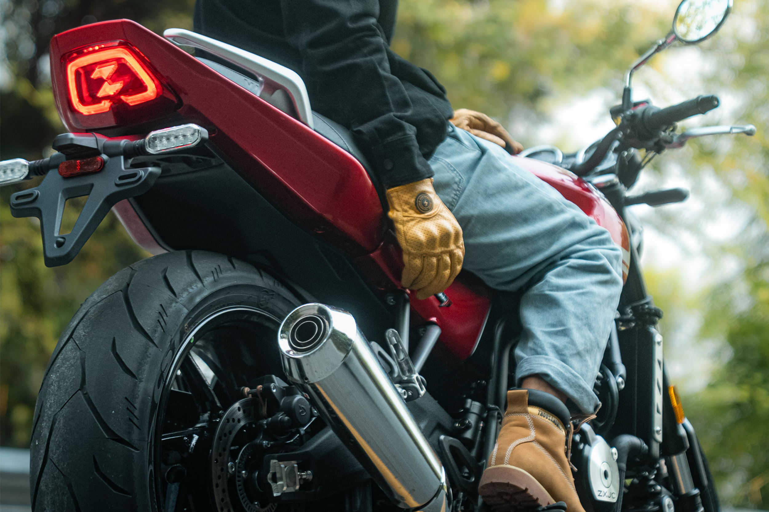 Rear three-quarter close-up of a red 500F showing an illuminated tail light, silver exhaust and rider wearing tan boots.