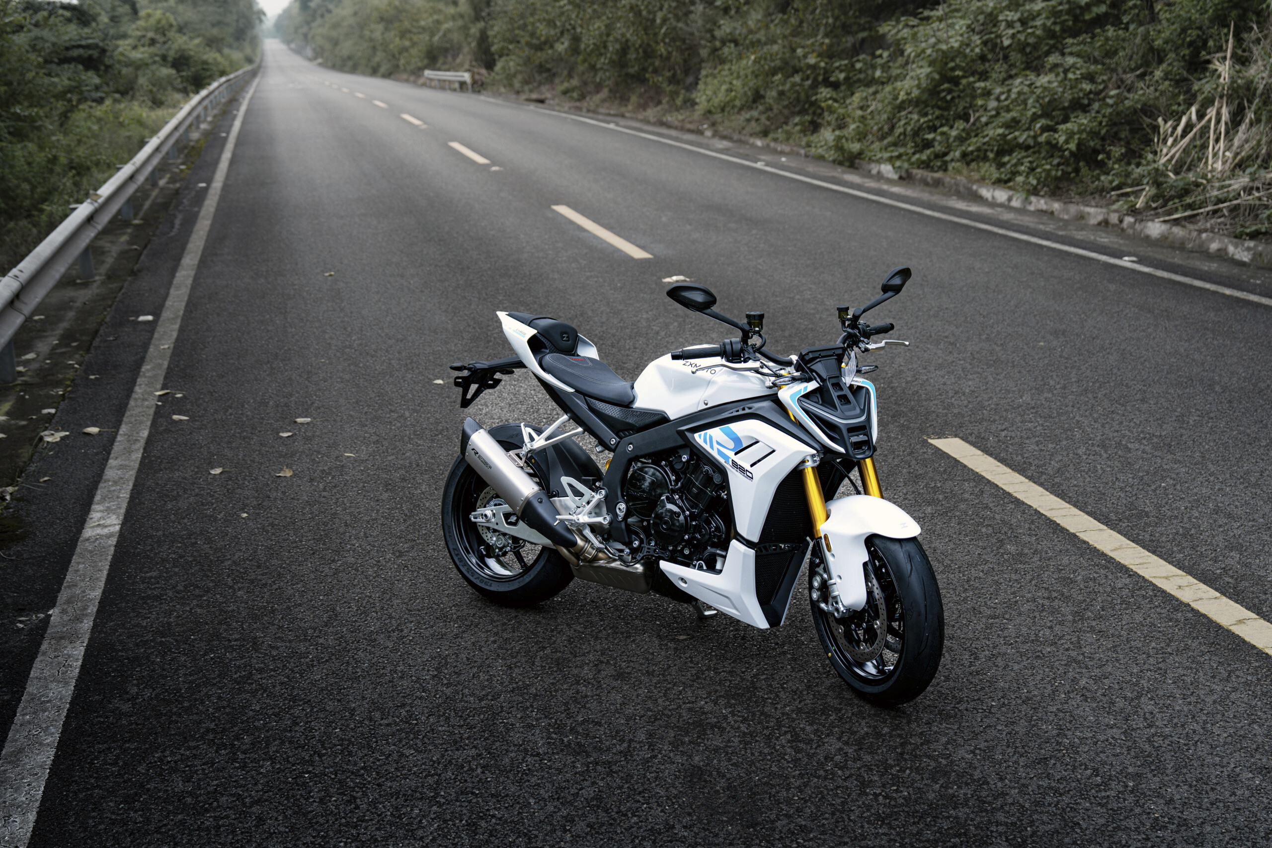 White ZXMOTO 820R parked on an empty tree-lined road beside a metal guardrail.