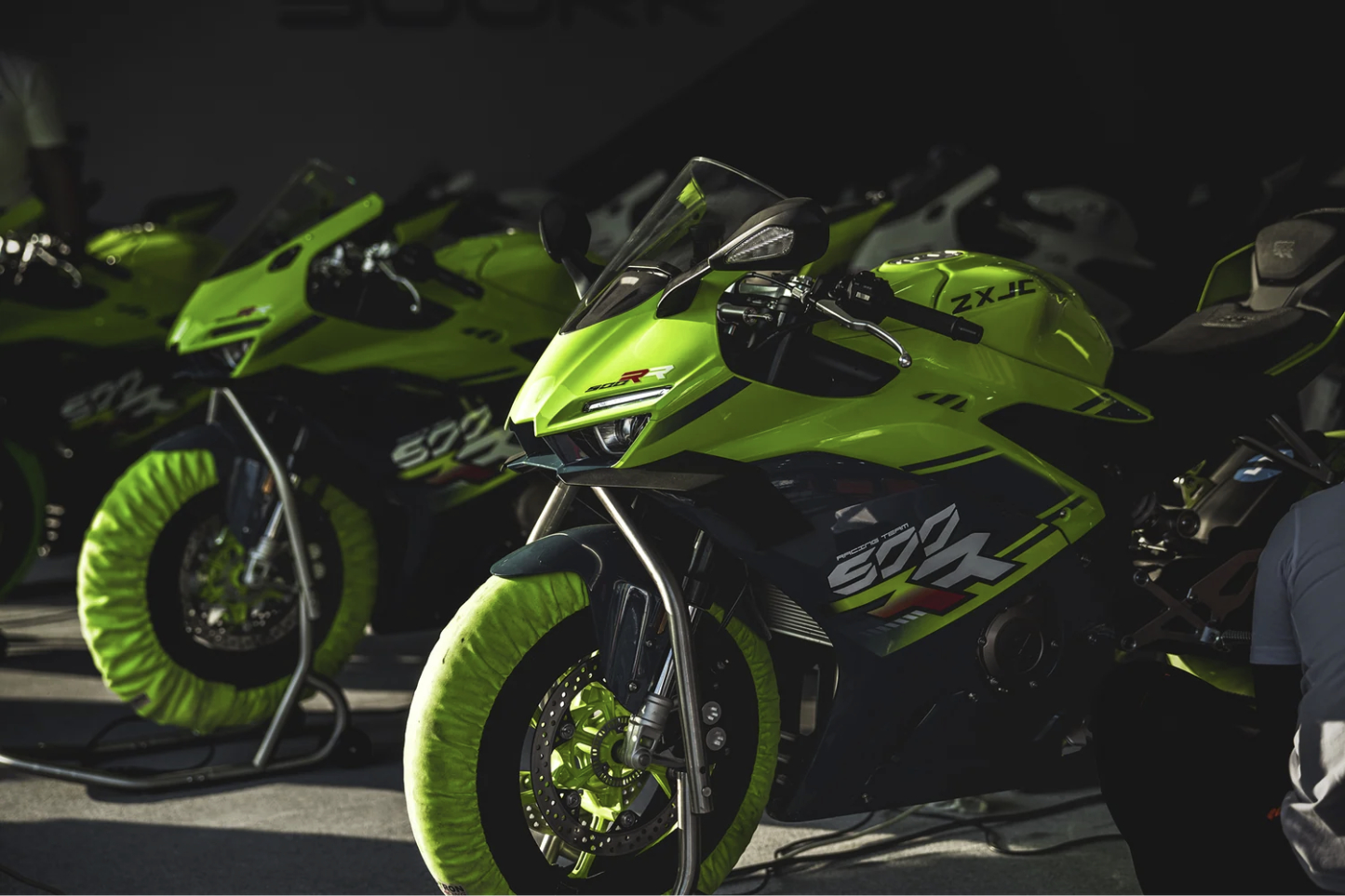 ZX Moto 500RR sportbikes lined up in a garage on paddock stands with tyre warmers fitted.