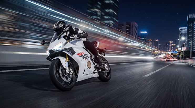 Rider on a white ZX Moto 500RR travelling along a city road at night with blurred lights behind.