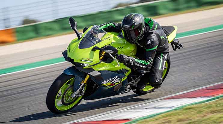 Rider in black and green leathers cornering a lime green ZX Moto sportbike beside circuit kerbing.